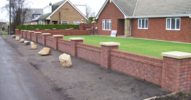Low red-brick garden wall with cream coping stones and pillar caps