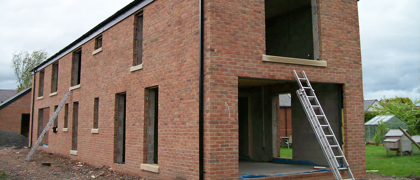 Two-storey red-brick new build with open window openings and ladders on site