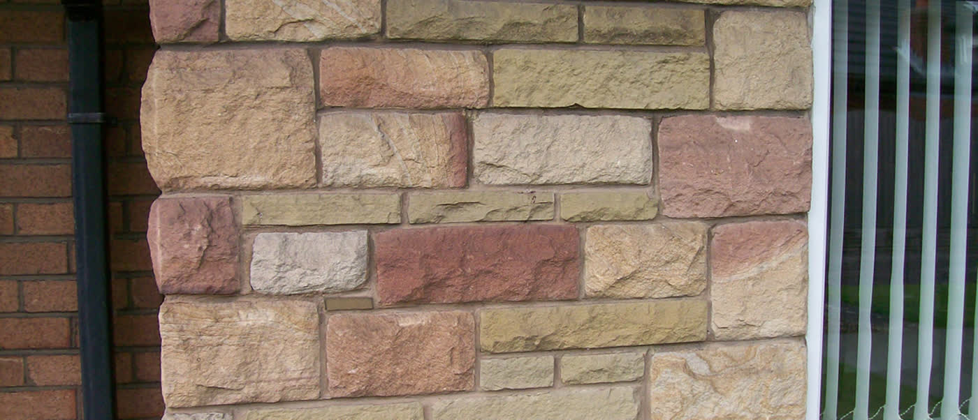 Split-face stone wall meeting red brick beside a white window